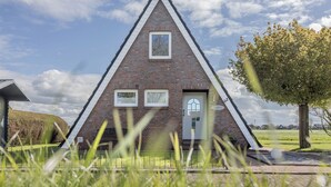 Een drielingsvormig bakstenen gebouw met een deur en twee ramen, omgeven door gras en een boom.