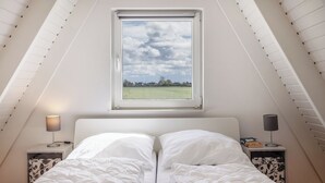 Een slaapkamer met een bed, twee nachtkastjes, een raam en uitzicht op een veld.