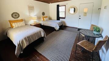 A bedroom with two beds, a ceiling fan, a small table with chairs, and a window with curtains.