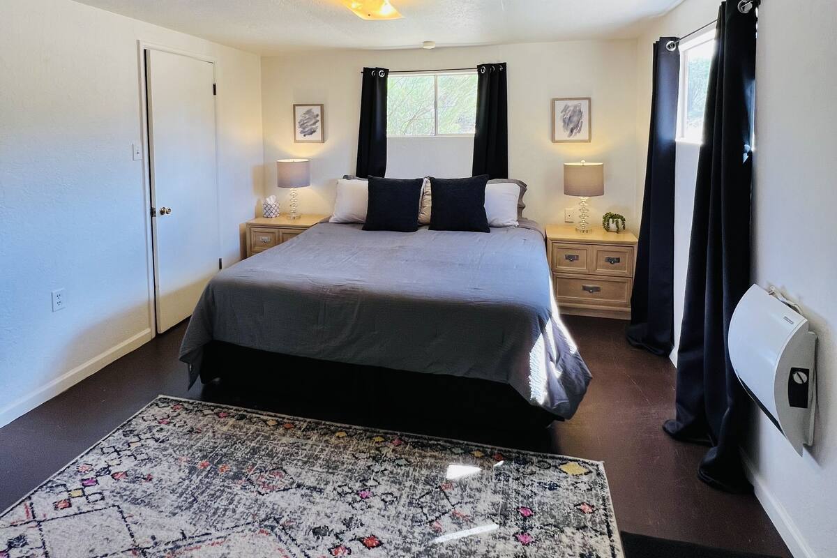 Un dormitorio con cama, mesitas de noche, una ventana con cortinas, una alfombra y un aire acondicionado de pared.