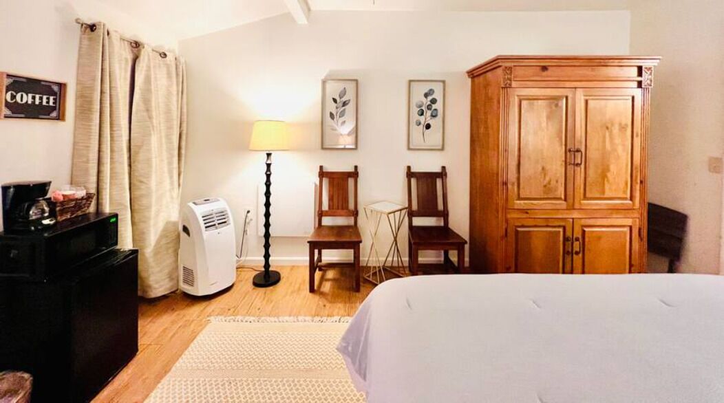 Une chambre à coucher comprenant un lit, une armoire en bois, un bureau avec une lampe et une machine à café.