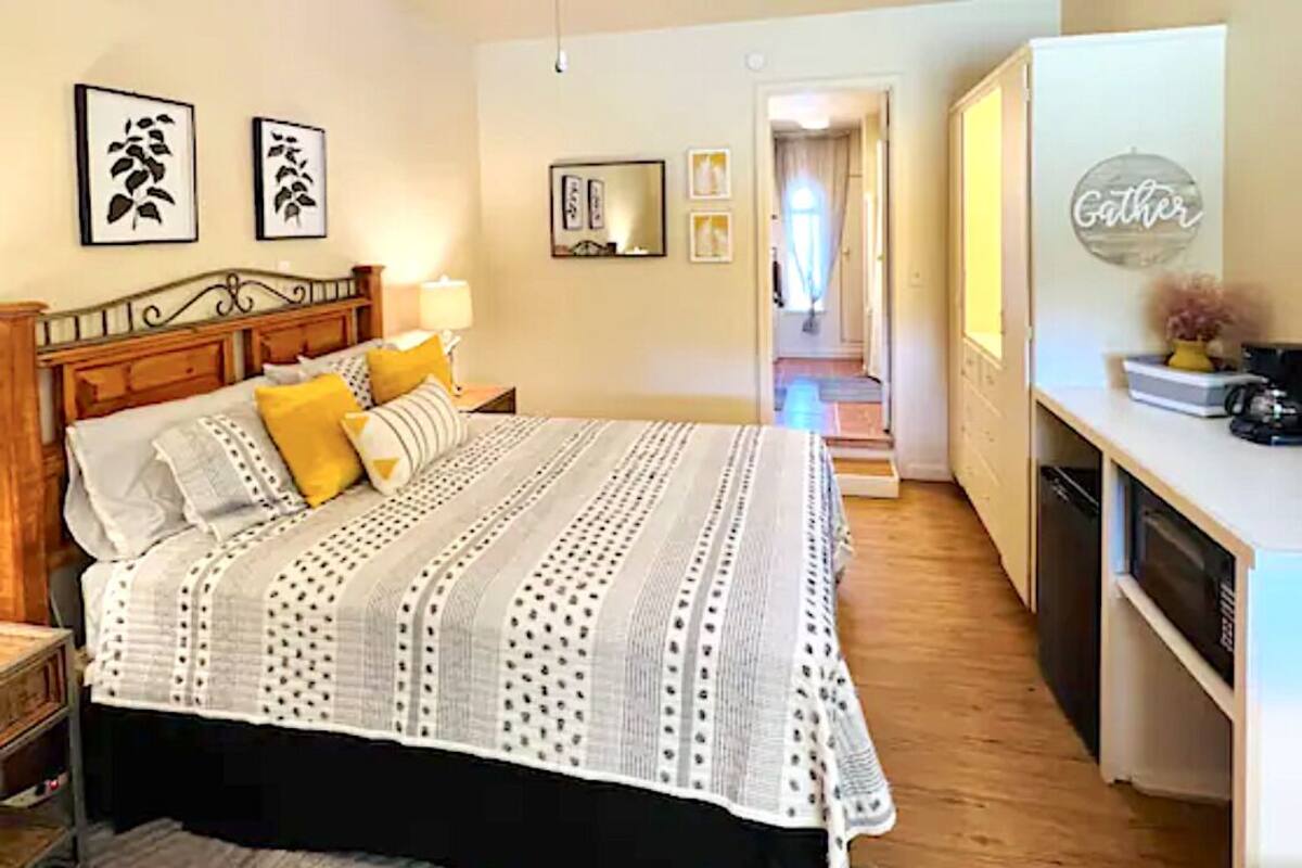 Un dormitorio con cama, mesitas de noche, cómoda, espejo y una pared decorada con cuadros.