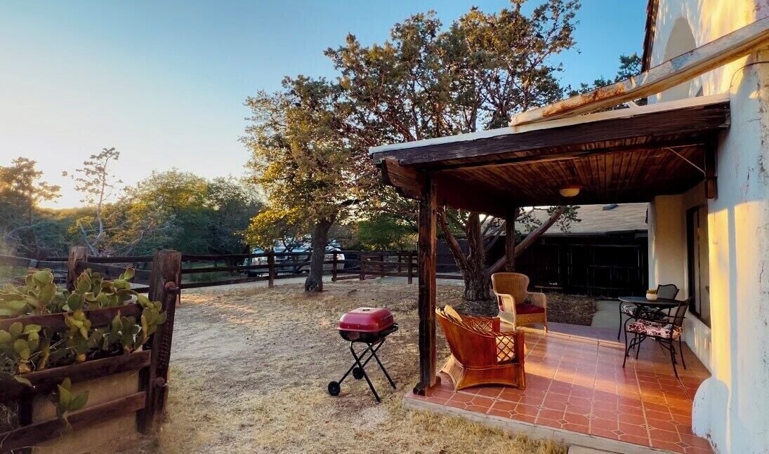 A covered patio area with a grill, outdoor furniture, and a view of a building.