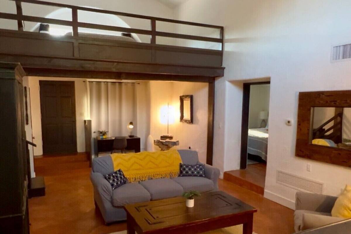 Amplia sala de estar con techo alto, ventilador de techo, sofá con cojines, mesa de centro y televisor.