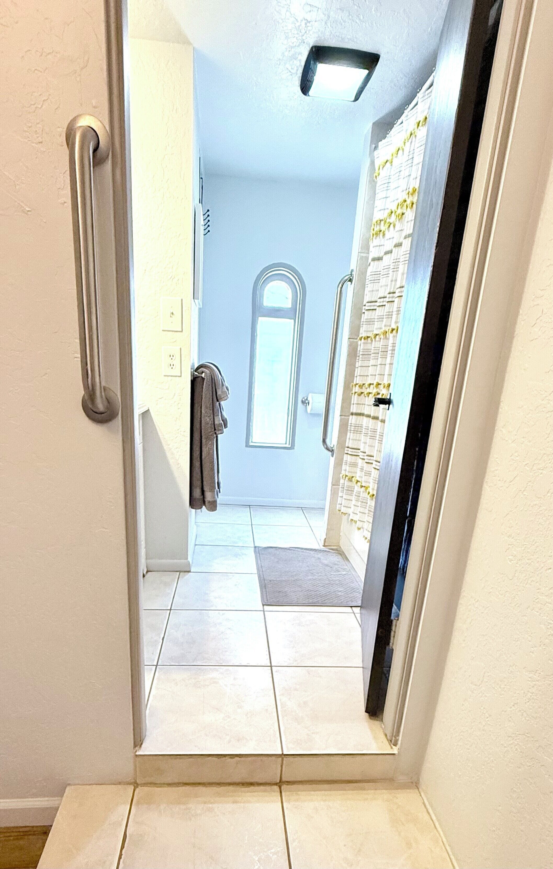 A narrow hallway with a door leading to a room with a large window and a door with a curtain.