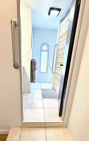 A narrow hallway with a door leading to a room with a large window and a door with a curtain.