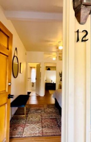 A hallway with a patterned rug, a wooden bench, and a door with a number '12' sign.