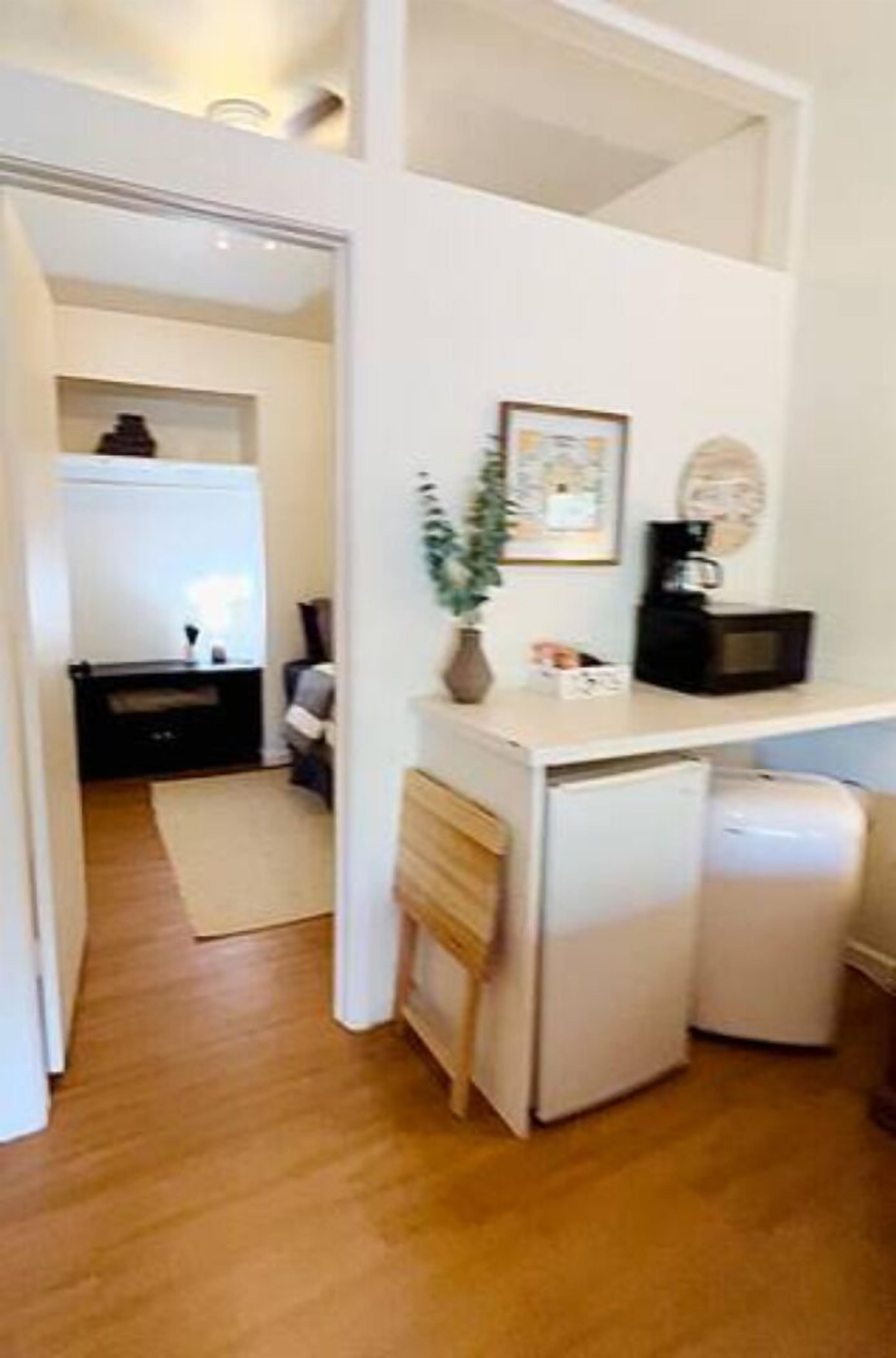 A compact kitchen with a microwave, a small refrigerator, and a sink. There is a plant on the counter and a framed picture on the wall.