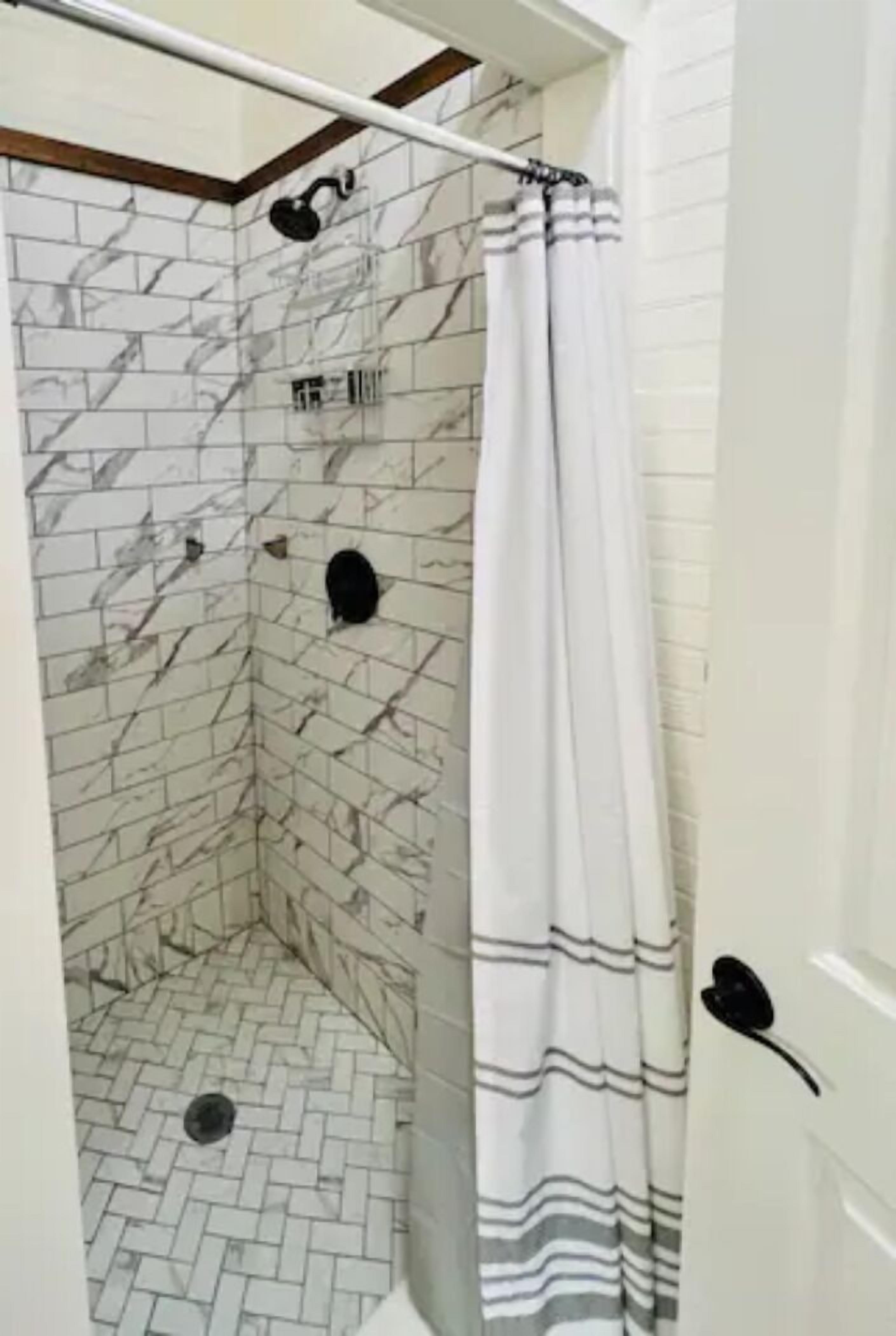 Una ducha con pared de azulejos blancos y cortina de baño a rayas.