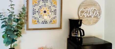 Una cocina con un cuadro de flores enmarco, una cafetera, un microondas y un letrero decorativo.