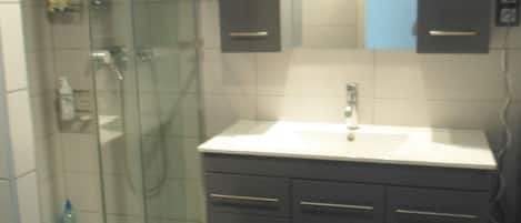 A bathroom with a glass shower enclosure, a sink, and dark-toned cabinets.