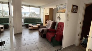 A living room with a green sofa, a red armchair, and a small table. There is a window with a view of trees and buildings. - Bright apartment in Balaruc-les-Bains, pets allowed (Balaruc-les-Bains)