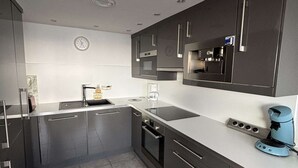 A modern kitchen with dark cabinetry, a built-in oven, a coffee maker, and a clock on the wall. - Bright apartment in Balaruc-les-Bains, pets allowed (Balaruc-les-Bains)