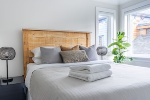 Una cama bien hecha con un cabecero de madera, una planta en maceta y dos lámparas a cada lado.