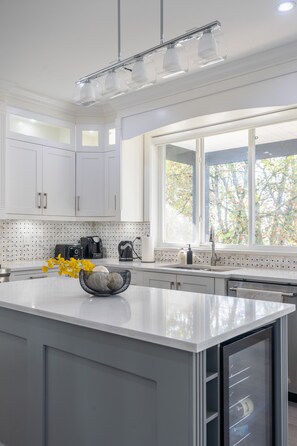 Una cocina moderna con armarios blancos, una isla grande y un ventanal con vista a árboles.