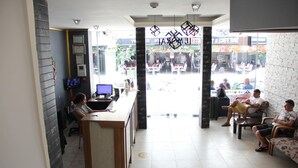 Zona de recepción con mostrador, computadora y área de descanso con personas.