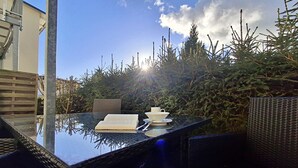 Een terras met een glazen tafel, rieten stoelen, een boek, een kopje en een schoteltje.