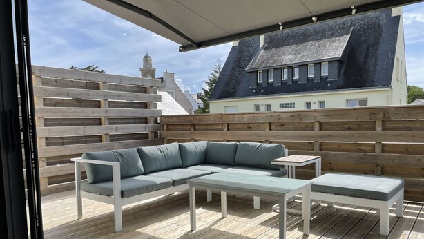 Eine Außenpatio mit Holzterrasse, einem grauen Ecksofa, einem kleinen Tisch und einer Bank.
