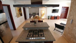 Une cuisine moderne dotée de plans de travail en granit, d’une cuisinière à gaz et d’un four encastré. On y trouve également un coin repas avec une table et des chaises, ainsi qu’un téléviseur fixé au mur.