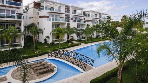 Un hôtel moderne doté de nombreux balcons, d’une piscine centrale et d’un aménagement paysager luxuriant.