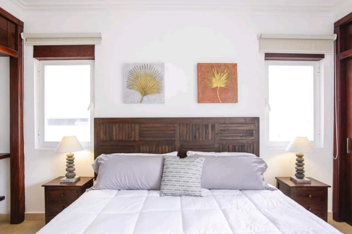 Une chambre à coucher avec un grand lit, deux tables de chevet, une tête de lit en bois et deux lampes fixées au mur.