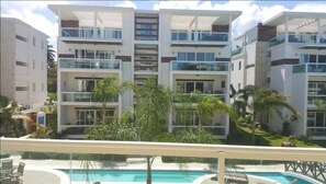 A modern multi-story hotel with balconies, a pool area, and lush landscaping.