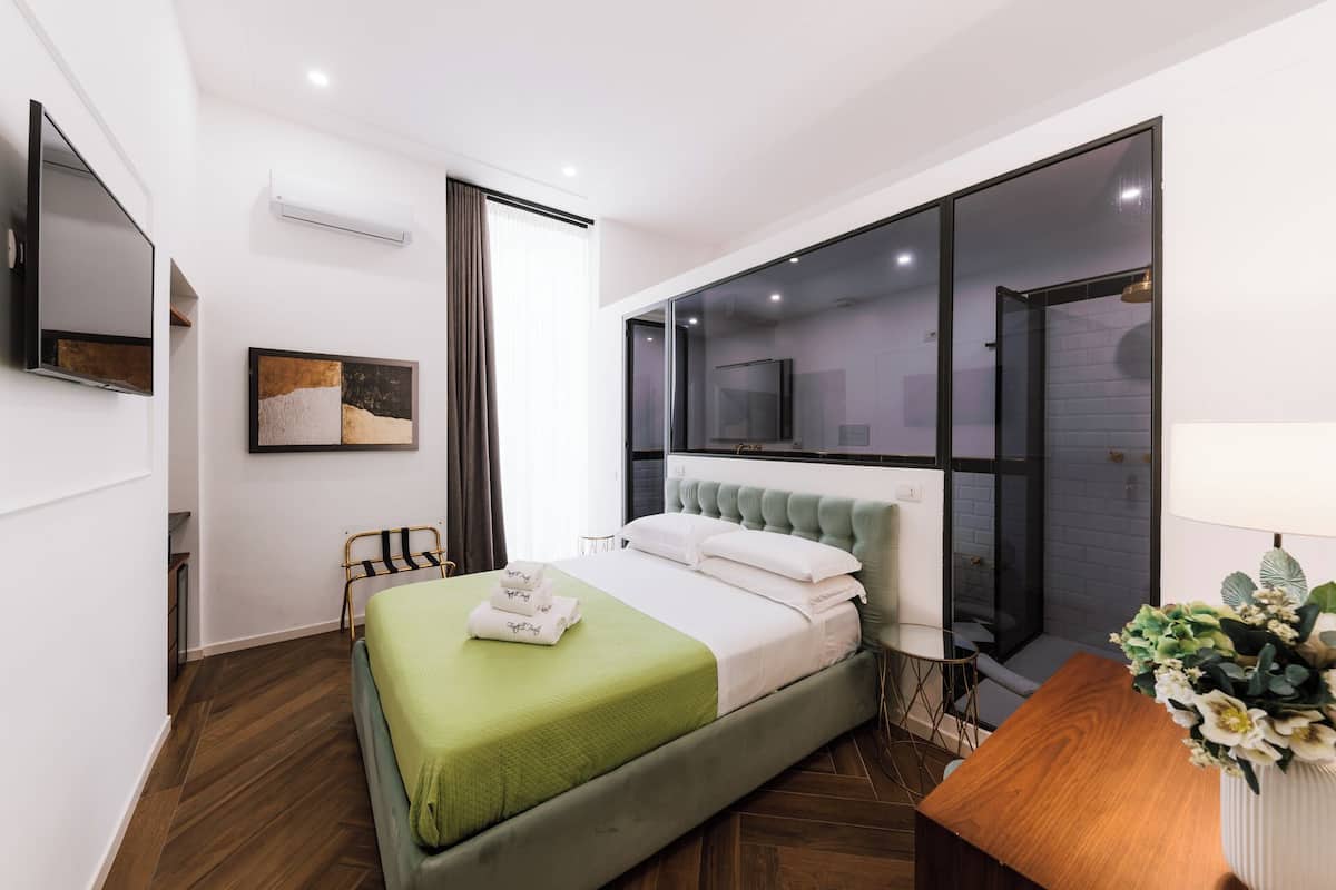 A modern bedroom with a green bed, a wooden nightstand, a TV, and a large window.