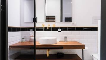 Un baño moderno con piso a cuadros blanco y negro, un tocador de madera con lavamanos blanco e accesorios dorados.