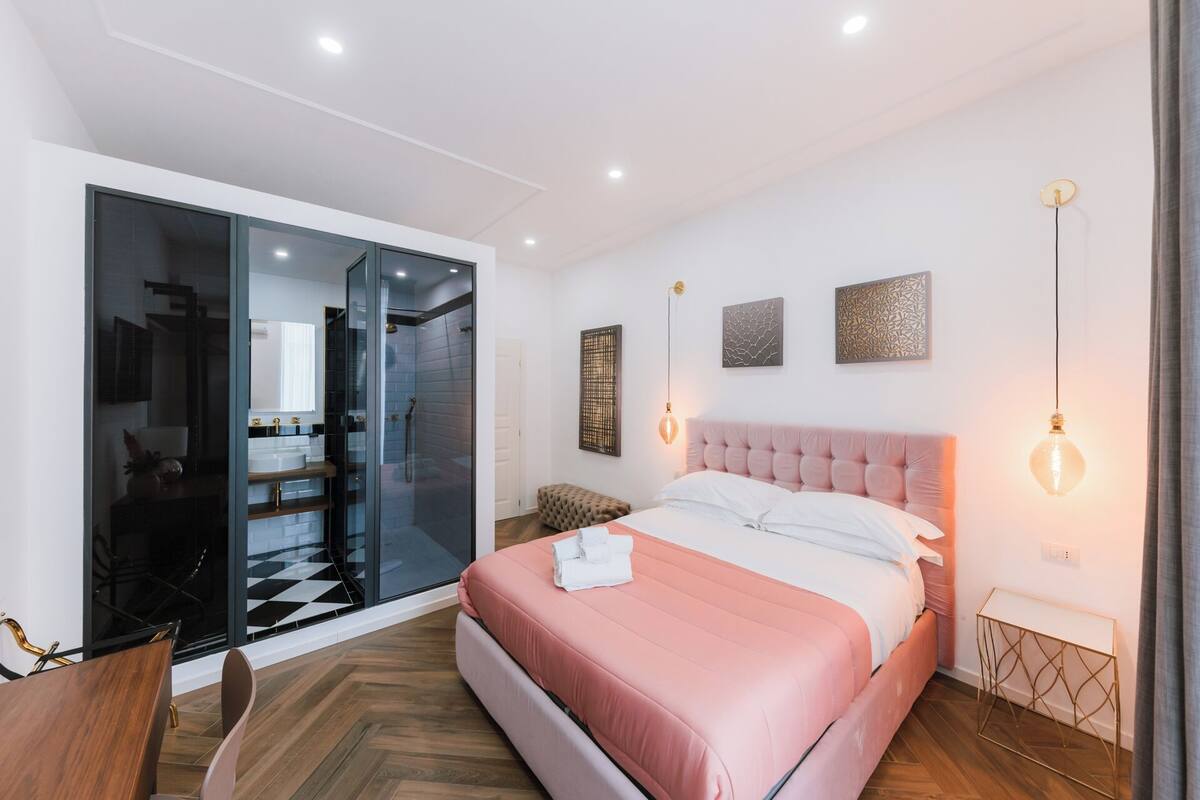 A modern bedroom with a large bed, a glass-enclosed shower, and a small seating area.