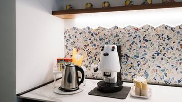 A kitchen with a coffee machine, a kettle, and a stack of disposable cups on a countertop.