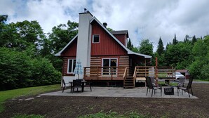 Una cabaña con terraza de madera, mobiliario exterior y vistas a un área boscosa.