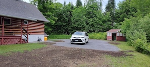 Eine Holzhütte mit einem Schotterweg, der zu einem weißen SUV davor führt.