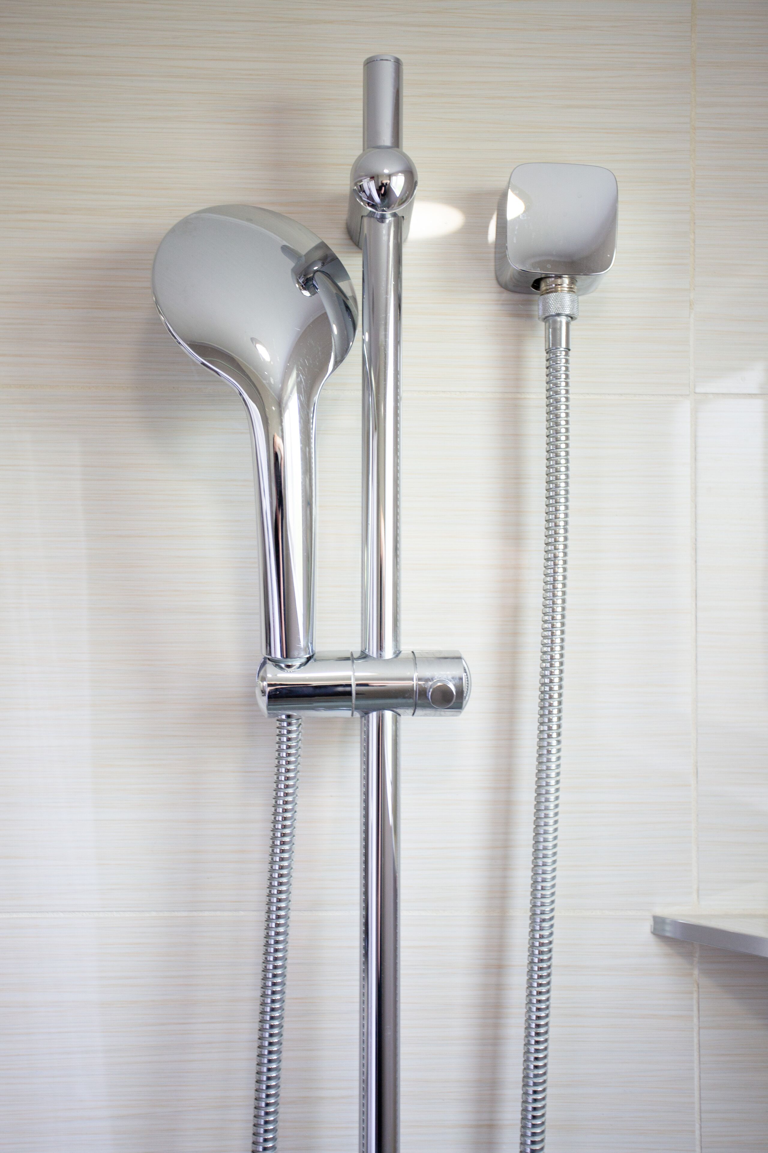 A chrome showerhead with a flexible hose and a separate handheld showerhead mounted on the wall.