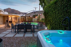 An outdoor patio with a hot tub, seating area, and a view of mountains.