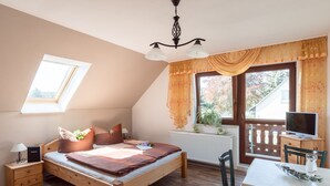 Un dormitorio con una cama de madera, un escritorio con computadora, una silla, una ventana con cortinas y un radiador.