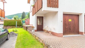 Ein zweigeschossiges Wohnhaus mit befestigter Auffahrt, einer Holztür und einer kleinen Außenbereich-Sitzgelegenheit mit Tisch und Stühlen.