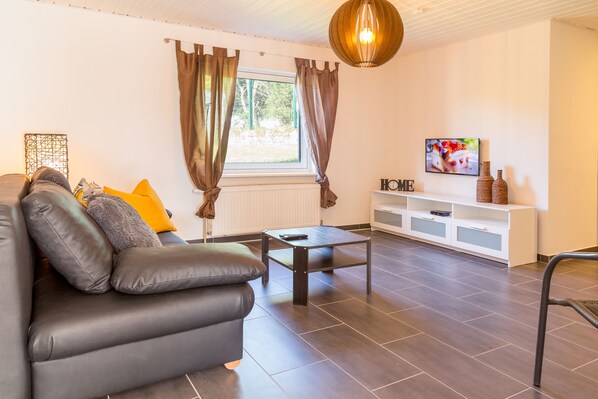 A modern living room with a sofa, a coffee table, and a TV on a white shelf. - Cozy modern apartment with local transport (Wald-Michelbach)