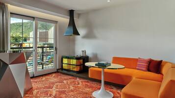 A modern living room with a sofa, a round table, and a large window with a view of a building and hills.