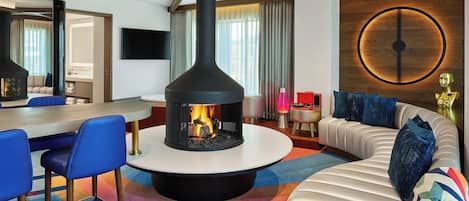 A modern living room with a central fireplace, a sofa, a dining area, and a large mirror.