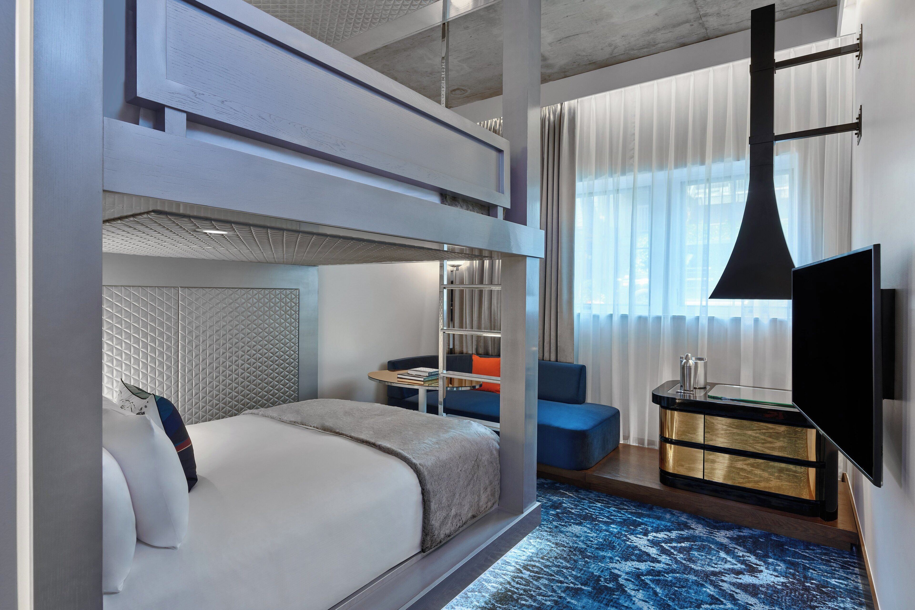 Ein modernes Hotelzimmer mit Etagenbett, Schreibtisch und Flachbildfernseher sowie einer Sitzecke mit blauem Sofa.