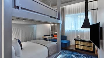 Een moderne hotelkamer met een stapelbed, een bureau met een flatscreen televisie en een zithoek met een blauwe bank.