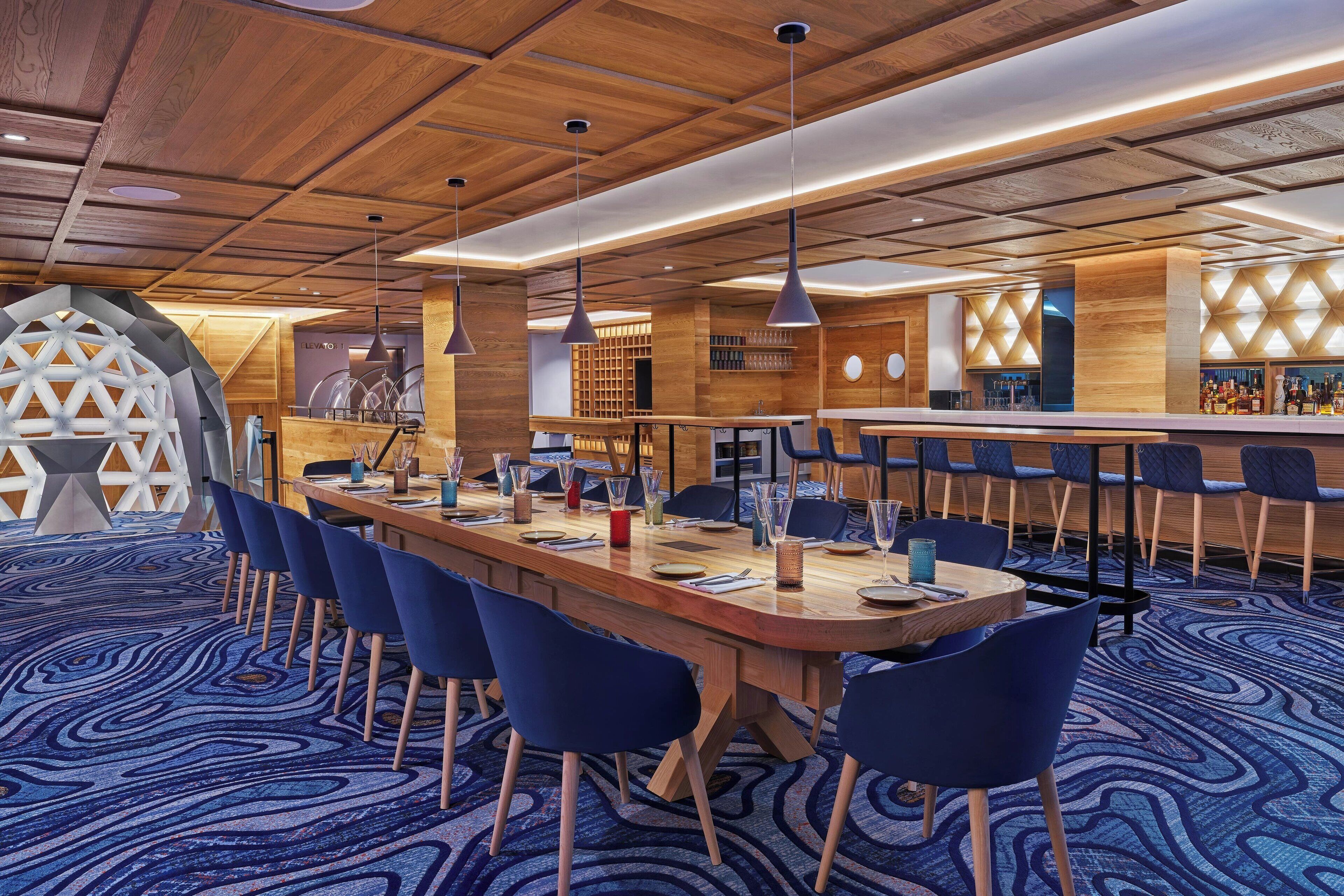Un hall d’hôtel moderne avec un long comptoir d’accueil en bois, des chaises bleues et une moquette à motifs.