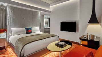 A modern hotel room with a large bed, a bedside table with a lamp, a TV mounted on the wall, and a red sofa.