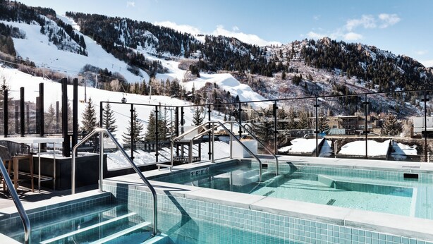 A pool area with steps leading into the water, surrounded by a metal railing and a view of snow-covered mountains. - W Aspen (Aspen)