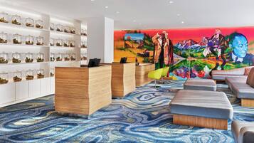 A hotel lobby with a reception desk, seating area, and a wall with glass jars containing plants.