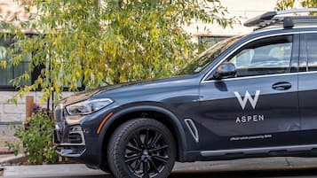 A black SUV with the Aspen logo on the side, parked on a street with a tree and building in the background.