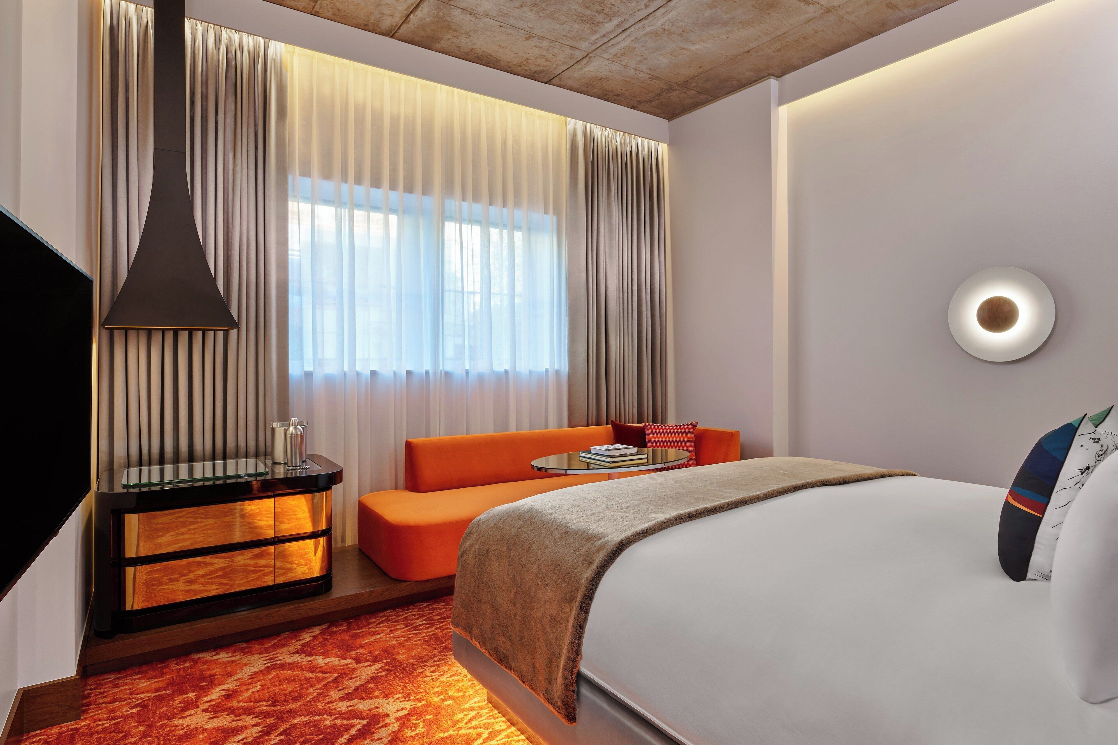 Een moderne hotelkamer met een groot bed, een oranje sofa en een glazen bijzettafeltje.