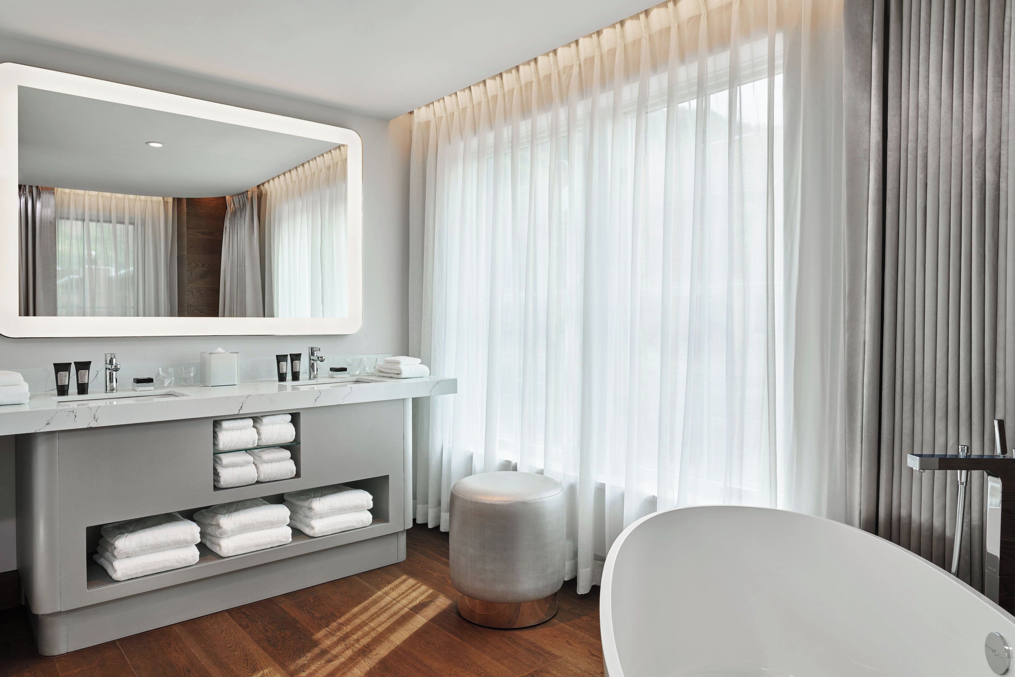 Ein modernes Badezimmer mit großem Spiegel, Waschtisch mit Pflegeprodukten, einer Badewanne und Holzboden.