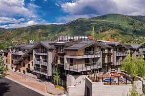 A modern multi-story hotel with balconies, a rooftop pool, and a mountainous backdrop. - W Aspen (Aspen)