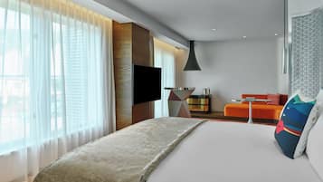 A modern hotel room with a large bed, a flat-screen TV, a sofa, and a dining table.